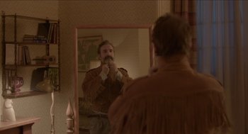 Movie still from “Deerskin” (2019), directed by Quentin Dupieux – A man is looking at himself in the mirror; Medium shot, Over the shoulder angle