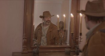 Movie still from “Deerskin” (2019), directed by Quentin Dupieux – A man wearing a cowboy hat looking into a mirror; Medium shot, Low angle