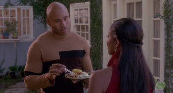 Movie still from “Deliver Us from Eva” (2003), directed by Gary Hardwick – A man in a brown shirt is serving a plate of food to a woman in a red dress; Medium shot, Over the shoulder angle
