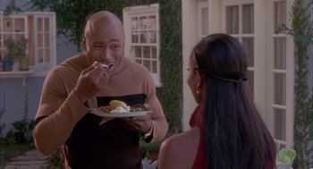 Movie still from “Deliver Us from Eva” (2003), directed by Gary Hardwick – A man eating a plate of food while a woman looks on; Medium shot, Over the shoulder angle