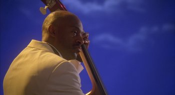 Movie still from “Deliver Us from Eva” (2003), directed by Gary Hardwick – A man holding a large contrabass in front of a blue sky; Close Up shot, Low angle