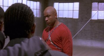 Movie still from “Deliver Us from Eva” (2003), directed by Gary Hardwick – A man with a chain around his neck is looking at another man; Medium shot, Over the shoulder angle