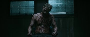 Movie still from “Deliver Us from Evil” (2014), directed by Scott Derrickson – A shirtless man sitting in a chair covered in graffiti; Medium shot, High angle