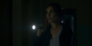 Movie still from “Demonic” (2021), directed by Neill Blomkamp – A woman is holding a flashlight in a dark room; Close Up shot, Low angle