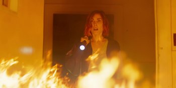 Movie still from “Demonic” (2021), directed by Neill Blomkamp – A woman holding a flashlight in front of a fire; Medium shot, Low angle
