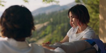 Movie still from “Demonic” (2021), directed by Neill Blomkamp – A woman sitting on top of a bench holding a plate of food; Close Up shot, Over the shoulder angle