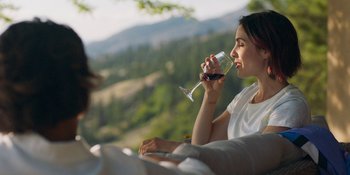 Movie still from “Demonic” (2021), directed by Neill Blomkamp – A woman drinking a glass of red wine from a wine glass; Medium shot, Over the shoulder angle