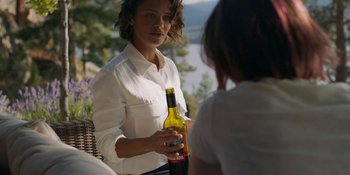 Movie still from “Demonic” (2021), directed by Neill Blomkamp – A woman holding a bottle of wine in her hand; Medium shot, Over the shoulder angle