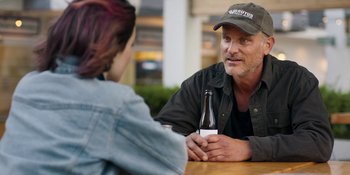 Movie still from “Demonic” (2021), directed by Neill Blomkamp – A man sitting at a table with a bottle of beer in front of a woman; Close Up shot, Over the shoulder angle