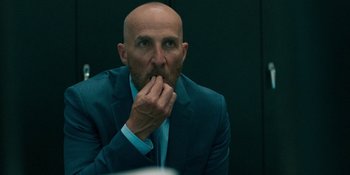 Movie still from “Demonic” (2021), directed by Neill Blomkamp – A man in a suit and tie sitting in front of a wall; Close Up shot, Low angle