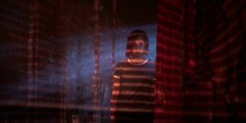 Movie still from “Demonic” (2021), directed by Neill Blomkamp – A man standing in front of a window with red curtains; Medium shot, Over the shoulder angle