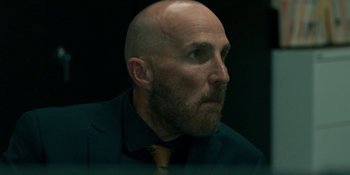 Movie still from “Demonic” (2021), directed by Neill Blomkamp – A man with a bald head wearing a suit and tie; Close Up shot, Low angle