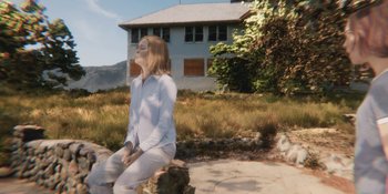 Movie still from “Demonic” (2021), directed by Neill Blomkamp – A woman sitting on top of a rock in front of a house; Wide shot, Low angle
