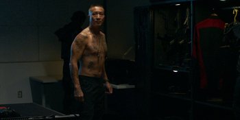 Movie still from “Demonic” (2021), directed by Neill Blomkamp – A man standing in the dark with a tattoo on his chest; Medium shot, Over the shoulder angle