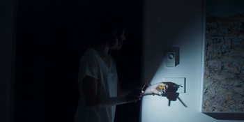 Movie still from “Demonic” (2021), directed by Neill Blomkamp – A woman standing in a dark room holding a cell phone; Medium shot, Low angle