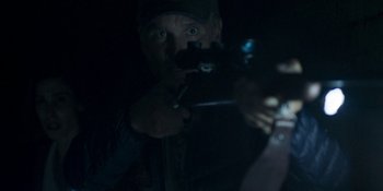 Movie still from “Demonic” (2021), directed by Neill Blomkamp – A man is holding a gun in the dark; Close Up shot, Over the shoulder angle