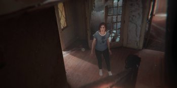 Movie still from “Demonic” (2021), directed by Neill Blomkamp – A woman standing in a room in front of an open door; Wide shot, High angle
