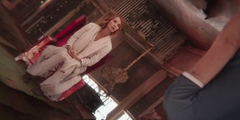 Movie still from “Demonic” (2021), directed by Neill Blomkamp – A woman sitting on a red chair in a room; Wide shot, Over the shoulder angle