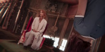 Movie still from “Demonic” (2021), directed by Neill Blomkamp – A woman sitting on a red chair in a room; Medium shot, Over the shoulder angle