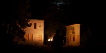Movie still from “Demonic” (2021), directed by Neill Blomkamp – A man standing in front of a fire at night; Extreme Wide shot, Low angle