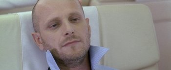 Movie still from “Demonlover” (2002), directed by Olivier Assayas – A man with a bald head sitting in a chair; Close Up shot, Low angle