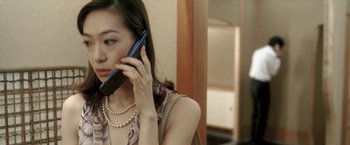 Movie still from “Demonlover” (2002), directed by Olivier Assayas – A woman is talking on a cell phone while wearing pearls; Close Up shot, High angle