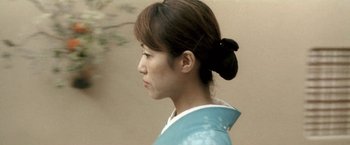 Movie still from “Demonlover” (2002), directed by Olivier Assayas – A young woman wearing a blue dress and a black hair bun; Close Up shot, Low angle