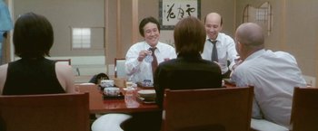 Movie still from “Demonlover” (2002), directed by Olivier Assayas – Three people sitting at a table with food; Medium shot, Over the shoulder angle