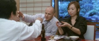 Movie still from “Demonlover” (2002), directed by Olivier Assayas – A group of people sitting at a table with drinks; Medium shot, Over the shoulder angle