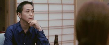 Movie still from “Demonlover” (2002), directed by Olivier Assayas – A man sitting in front of a bottle of beer; Close Up shot, Over the shoulder angle