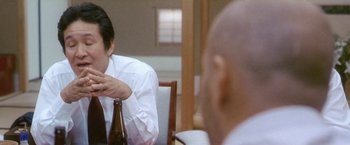 Movie still from “Demonlover” (2002), directed by Olivier Assayas – A man sitting at a table with a beer in his hand; Close Up shot, Over the shoulder angle