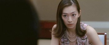 Movie still from “Demonlover” (2002), directed by Olivier Assayas – A person wearing a dress and pearls; Close Up shot, Over the shoulder angle