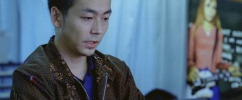 Movie still from “Demonlover” (2002), directed by Olivier Assayas – A man in a brown and blue jacket looking at the camera; Close Up shot, Over the shoulder angle