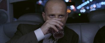 Movie still from “Demonlover” (2002), directed by Olivier Assayas – A man in a suit and tie drinking a glass of wine; Close Up shot, Low angle