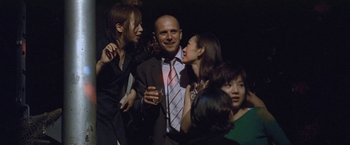 Movie still from “Demonlover” (2002), directed by Olivier Assayas – A group of people standing next to each other in a room; Medium shot, Over the shoulder angle