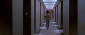 Movie still from “Demonlover” (2002), directed by Olivier Assayas – A woman walking down a long hallway in a building; Wide shot, Low angle