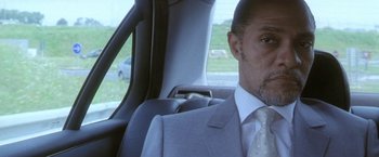 Movie still from “Demonlover” (2002), directed by Olivier Assayas – A person sitting in a car wearing a suit; Close Up shot, Low angle
