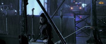 Movie still from “Demonlover” (2002), directed by Olivier Assayas – A woman in black jacket standing in front of a building; Medium shot, Low angle