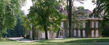 Movie still from “Demonlover” (2002), directed by Olivier Assayas – A large white building with a large tree in front of it; Extreme Wide shot, Low angle