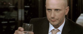 Movie still from “Demonlover” (2002), directed by Olivier Assayas – A man in a suit and tie holding a wine glass; Close Up shot, Low angle