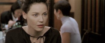 Movie still from “Demonlover” (2002), directed by Olivier Assayas – A young woman is looking at the camera while a young man is in the background; Close Up shot, Over the shoulder angle