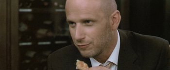Movie still from “Demonlover” (2002), directed by Olivier Assayas – A man in a suit and tie holding a piece of pizza; Extreme Close Up shot, Low angle