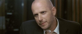 Movie still from “Demonlover” (2002), directed by Olivier Assayas – A man in a suit and tie looking at the camera; Close Up shot, Low angle