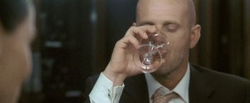Movie still from “Demonlover” (2002), directed by Olivier Assayas – A man in a suit and tie drinking a glass of wine; Close Up shot, Low angle