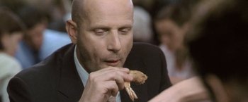 Movie still from “Demonlover” (2002), directed by Olivier Assayas – A man in a suit and tie eating a piece of food; Extreme Close Up shot, Low angle