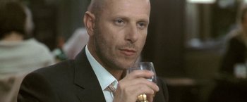 Movie still from “Demonlover” (2002), directed by Olivier Assayas – A man in a suit and tie holding a glass of wine; Close Up shot, Low angle