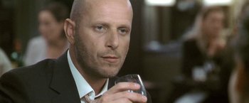 Movie still from “Demonlover” (2002), directed by Olivier Assayas – A bald man in a suit holding a glass of wine; Close Up shot, Low angle