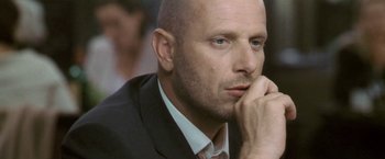 Movie still from “Demonlover” (2002), directed by Olivier Assayas – A man in a suit and tie holding his hand to his face; Close Up shot, Low angle