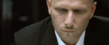 Movie still from “Demonlover” (2002), directed by Olivier Assayas – A person wearing a suit and tie; Extreme Close Up shot, Low angle