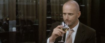 Movie still from “Demonlover” (2002), directed by Olivier Assayas – A man in a suit and tie holding a glass of wine; Close Up shot, Low angle